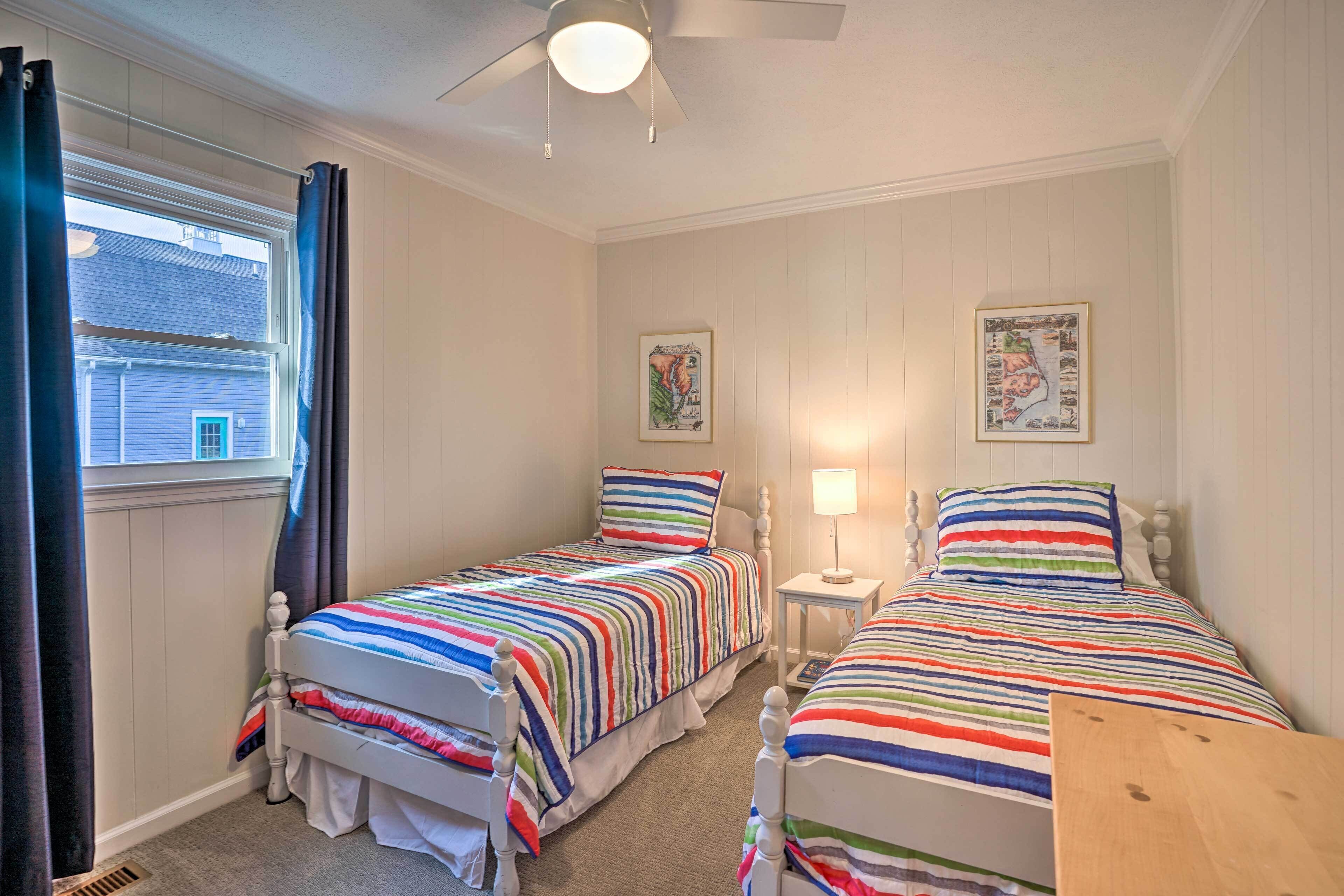A bedroom with two single beds, a ceiling fan, a window with curtains, and two wall-mounted lamps.