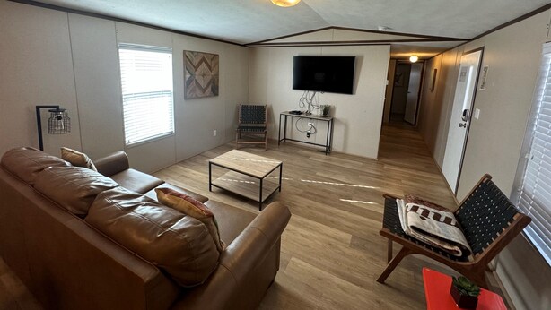A living room with a leather sofa, a coffee table, a TV, and a small table with a plant. - Red Sands Retreat D - 3 Bedroom 2 Bath (Moab)