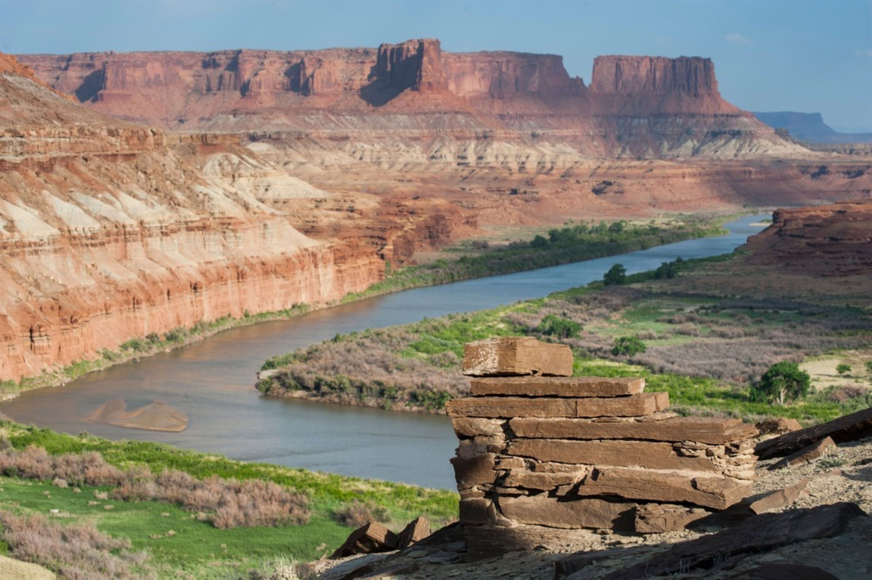 A river flowing through a canyon with layered rock formations and a stack of bricks in the foreground.
