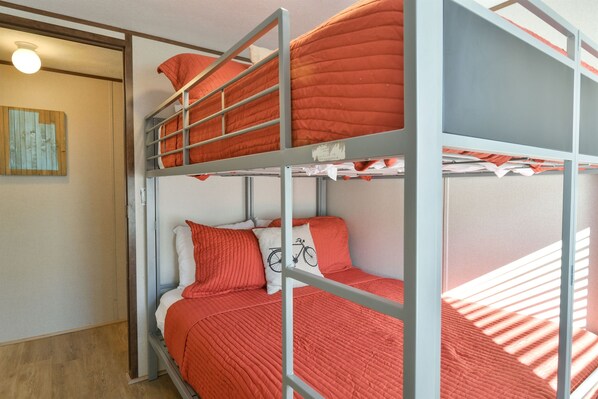 A bunk bed room with a wooden floor, a light switch, and a wall-mounted light fixture.