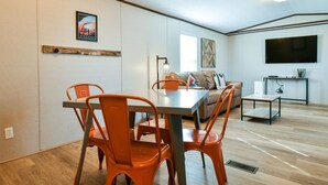 Un salon moderne avec un coin repas, comprenant un canapé, des fauteuils orange, une table et un téléviseur à écran plat.