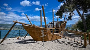 Una estructura de barco de madera con cerramiento de red, rodeada de grava y árboles.