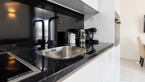 Una cocina moderna con una placa de inducción Bosch, un lavamanos de acero inoxidable y electrodomésticos negros.