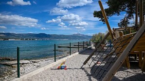 Un parque infantil con zona delimitada por red y vistas a un lago y montañas.