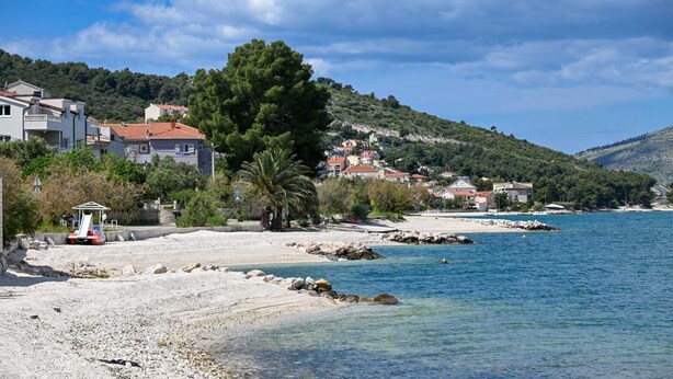 Una zona costera con playa de arena, costa rocosa y edificios con tejados rojos.