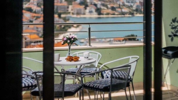 A balcony with a table set for two, chairs, a vase with flowers, and a view of a coastal town. - Apartment Jagoda near the beach (Okrug Gornji)