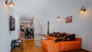A modern living room with a wooden floor, orange sofa, and wall-mounted lights. - Apartment Jagoda near the beach (Okrug Gornji)