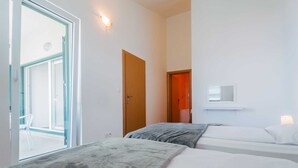 A hotel room with two beds, a window, a door, and a wall-mounted light fixture. - Apartment Jagoda near the beach (Okrug Gornji)