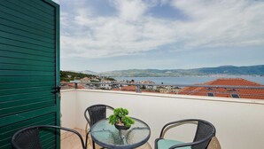 Ein Balkon mit Blick auf eine Küstenstadt, ein Tisch mit Topfpflanze und zwei Stühle.