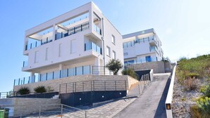 Un immeuble moderne à plusieurs étages, doté de balcons, d’une façade en pierre et d’un escalier menant à l’entrée.