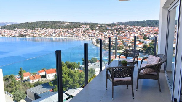 Un balcon avec des fauteuils en osier donnant sur une ville côtière et une étendue d’eau.
