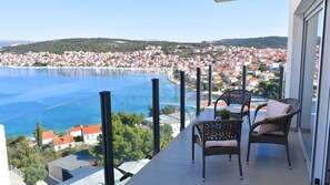 Un balcon avec des fauteuils en osier donnant sur une ville côtière et une étendue d’eau.