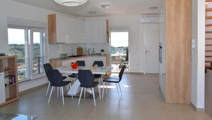 Une cuisine moderne avec des meubles blancs, une table à manger avec des chaises et une vue sur l’extérieur.
