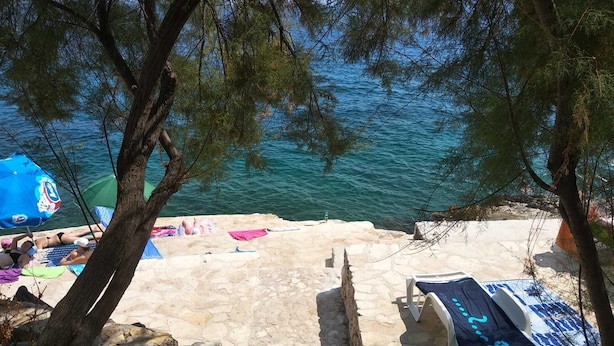 A stone staircase leading down to a beach with a view of the sea, a blue umbrella, and a boat. - Modern apartment Summer Joy near the beach (Okrug Gornji)