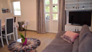 A living room with a sofa, a television, a dining area with chairs and a table, and a window with curtains. - Modern apartment Summer Joy near the beach (Okrug Gornji)