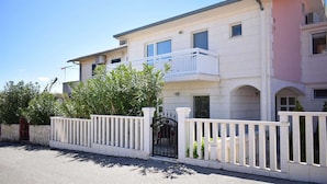 A two-story residential building with a balcony on the upper floor, a gated entrance, and a stone wall to the left. - Modern apartment Summer Joy near the beach (Okrug Gornji)