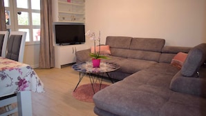 A living room with a sofa, a TV, a small table with a plant, and a dining area with chairs. - Modern apartment Summer Joy near the beach (Okrug Gornji)