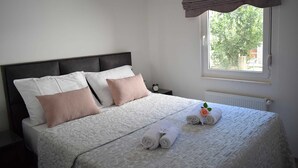 A neatly made bed with white and pink pillows, a rolled-up towel, and a small clock on a bedside table. - Modern apartment Summer Joy near the beach (Okrug Gornji)