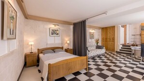A bedroom with a checkered floor, a bed with a wooden headboard, two bedside tables with lamps, a chair, and a wardrobe.