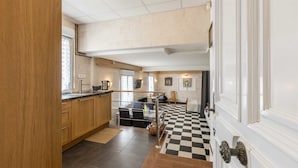 A modern kitchen with wooden cabinets, a black and white checkered floor, and a dining area with a table and chairs.