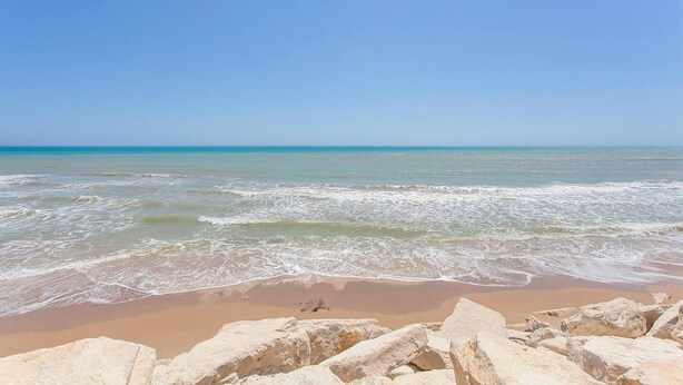 Une plage avec des vagues, un ciel dégagé et de gros rochers au premier plan.