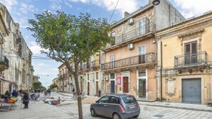 Une rue étroite bordée de bâtiments historiques, une voiture garée et un arbre.