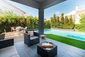 A covered patio area with outdoor furniture, a pool, and a well-maintained lawn.