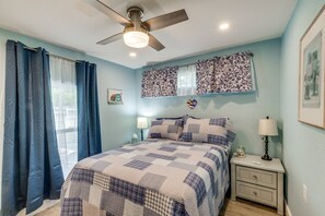 Une chambre à coucher avec un lit, un ventilateur de plafond, une table de chevet et une fenêtre avec des rideaux.