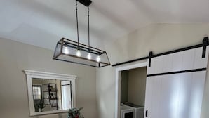 Spiseområde med et træbord, beige polstrede stole, en hængende lampe og en skydedør til skab.