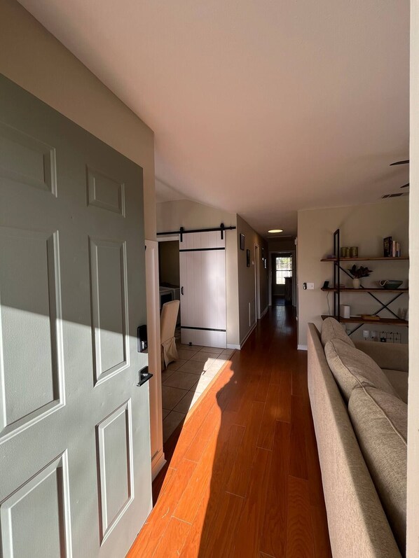 A hallway with a wooden floor, a grey door, a white wardrobe, a beige sofa, and a shelf with books and decorative items. - Modern home in prime location
(Brandon)