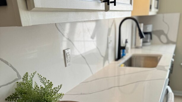 Et moderne køkken med en hvid marmor bordplade, en træbakke med en plante og en sæbeskål, samt en rustfri stålvask.