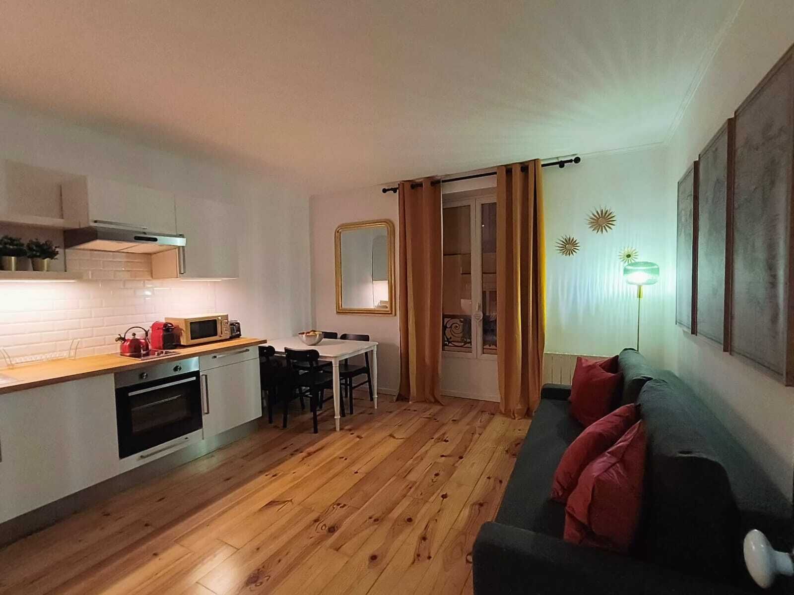 Ein kompakter Wohnbereich mit Küchenzeile, Essbereich und einer Sitzecke mit Sofa und Kissen.