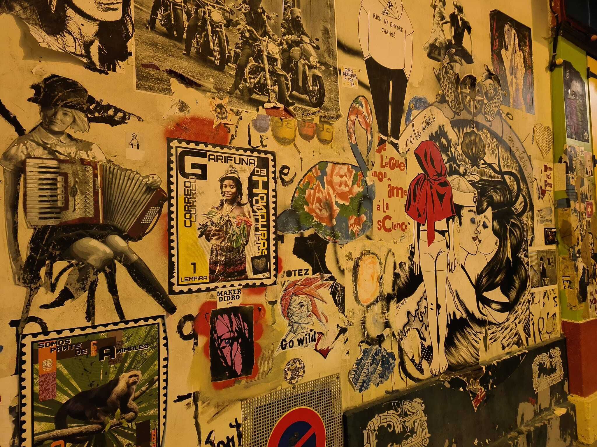 A wall covered with various stickers and posters, including a stamp from Honduras, a 'Go Wild' sticker, and a 'Wild' poster.