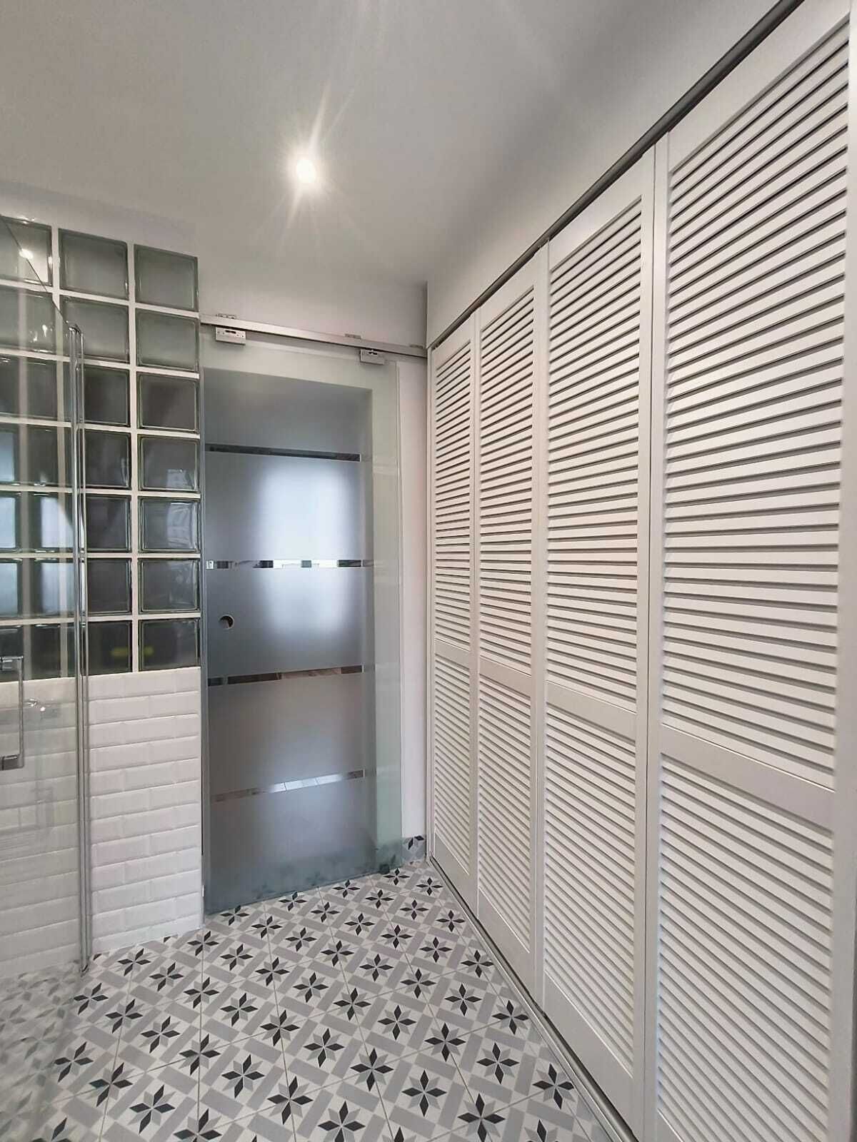 Een moderne badkamer met een douchecabine van glas, een betegelde vloer en een witte kast met verstelbare deuren.