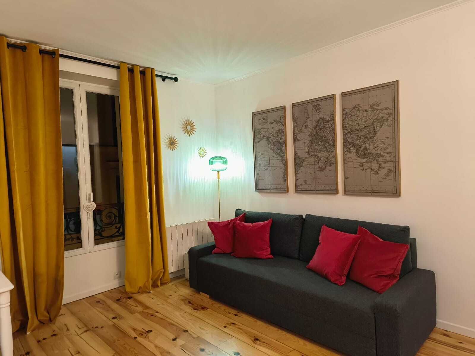 A living room with a dark green sofa, red cushions, a globe map on the wall, and a floor lamp.