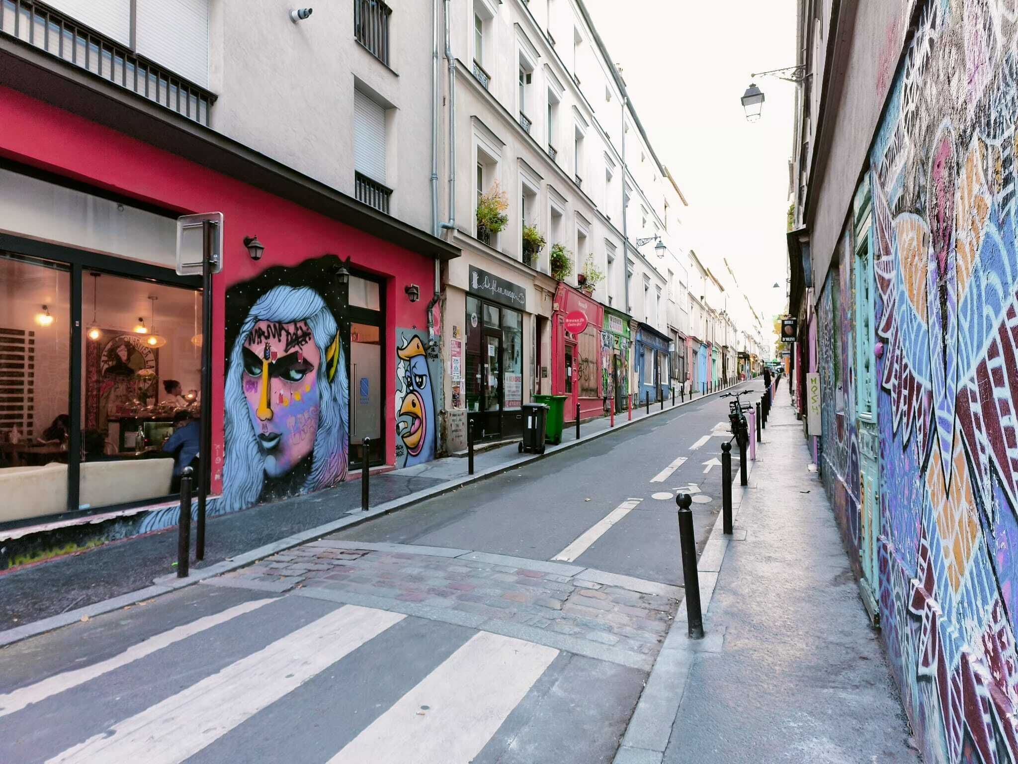 Une rue étroite, bordée de bâtiments des deux côtés, dont l’un est orné d’une grande fresque murale.