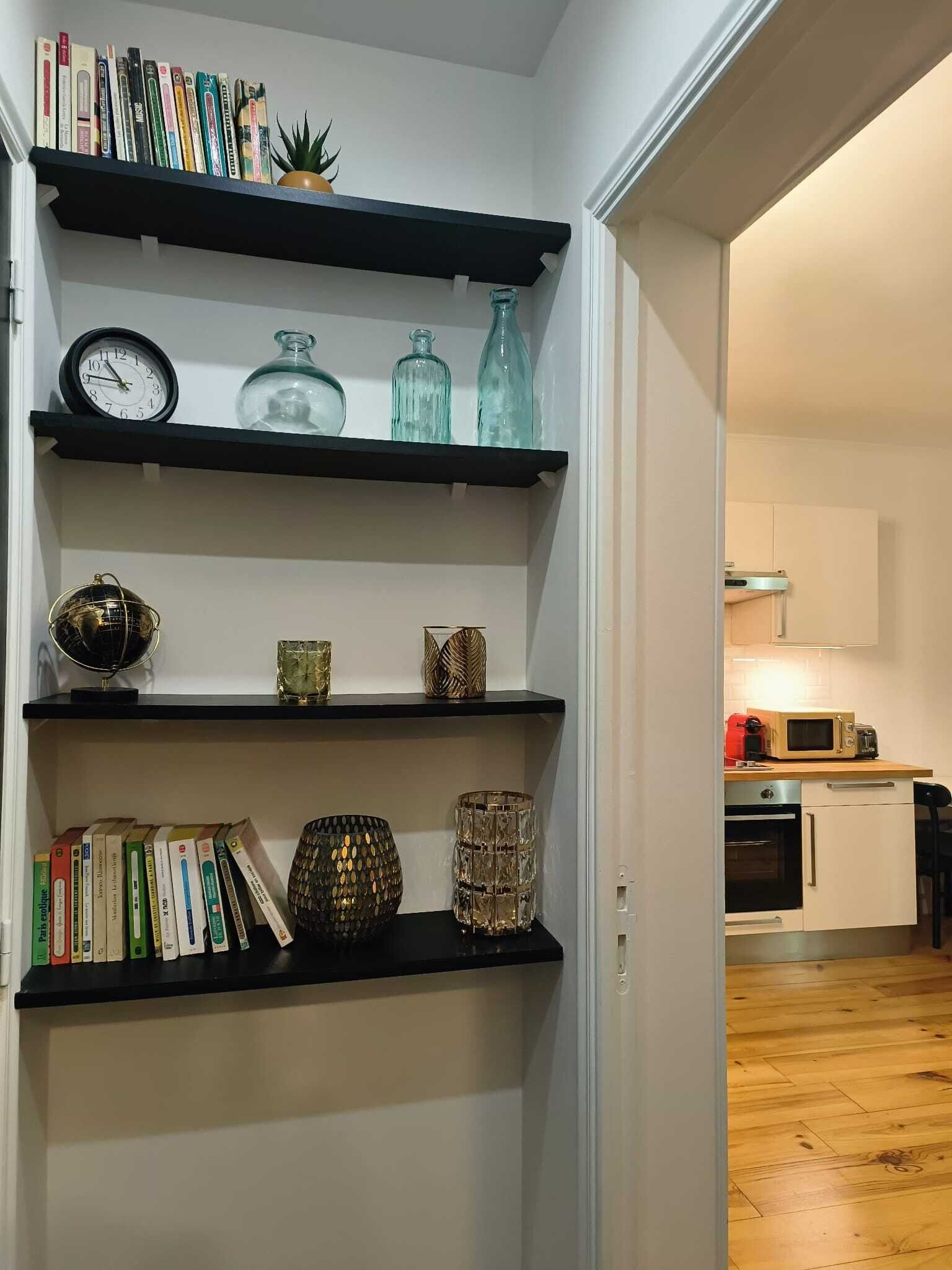 A hallway with black shelves holding books, decorative items, and a clock.