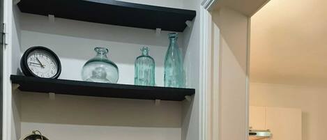 A hallway with black shelves holding books, decorative items, and a clock.