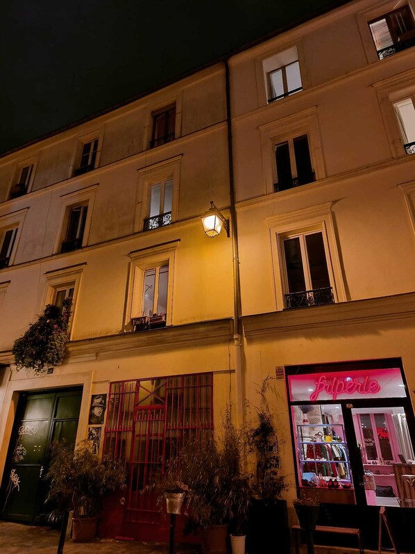 Un immeuble à plusieurs étages, avec un commerce situé au rez-de-chaussée appelé « fiperle » et une porte verte sur le côté gauche.
