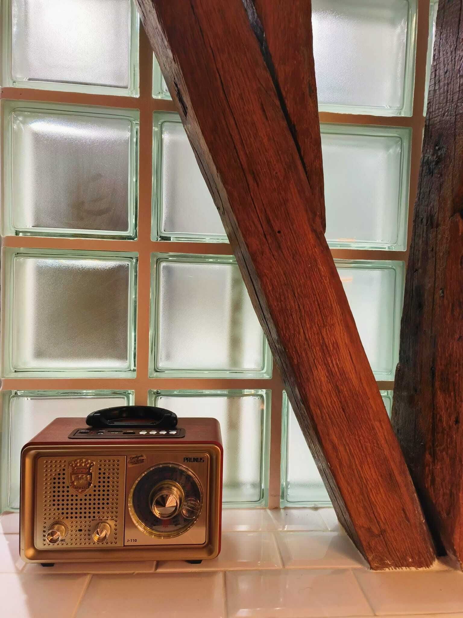 A vintage radio on a white surface with a wooden beam and frosted glass panels in the background.