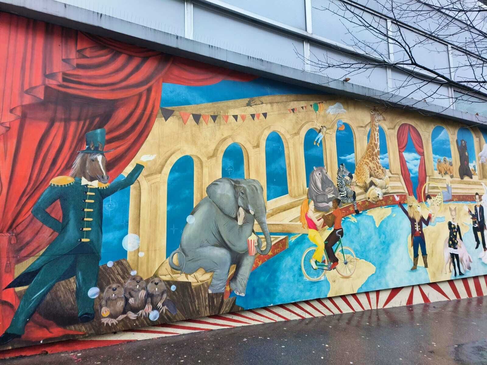 Un mural con diversas figuras y animales, incluyendo un elefante y un caballo, en una pared.