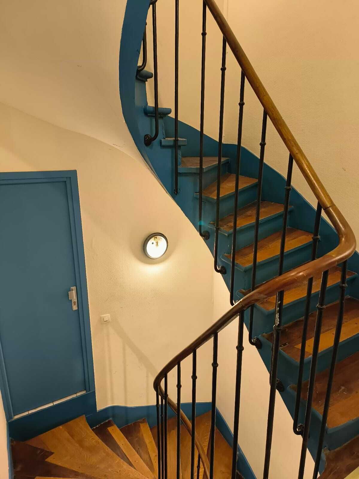 A spiral staircase with wooden steps and black railings, leading to a door with a light switch above it.