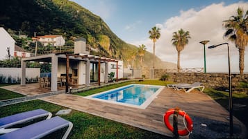 A modern outdoor pool area with lounge chairs, a lifebuoy, and a stone wall.