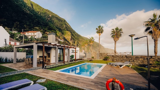 Un área de piscina moderna al aire libre con sillones de descanso, un flotador salvavidas y una pared de piedra.