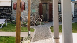 Un espacio al aire libre techado con pared de piedra, pérgola de madera y un camino que lleva a una puerta.