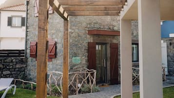 A covered outdoor area with a stone wall, wooden pergola, and a pathway leading to a door.