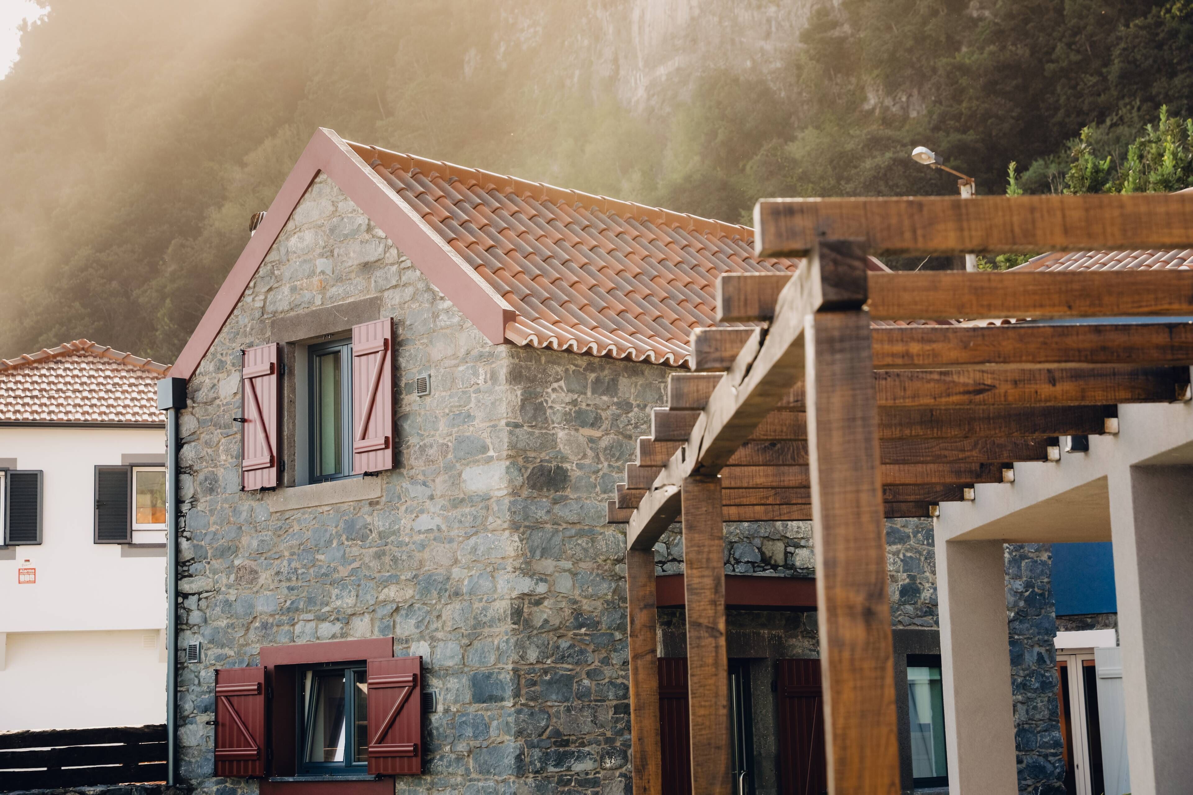 A stone building with a tiled roof and wooden pergola.