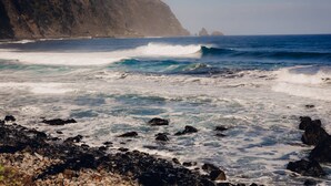 Una costa rocosa con olas rompiendo contra la orilla y un acantilado al fondo.