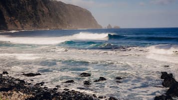A rocky coastline with waves crashing against the shore and a cliff in the background.