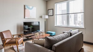 Un salon moderne avec un canapé, un fauteuil, une télévision et une grande fenêtre.
